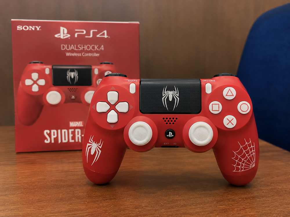 دسته بازی PS4 طرح Spider-Man قرمز با طراحی الهام‌گرفته از مرد عنکبوتی روی میز گیمینگ.